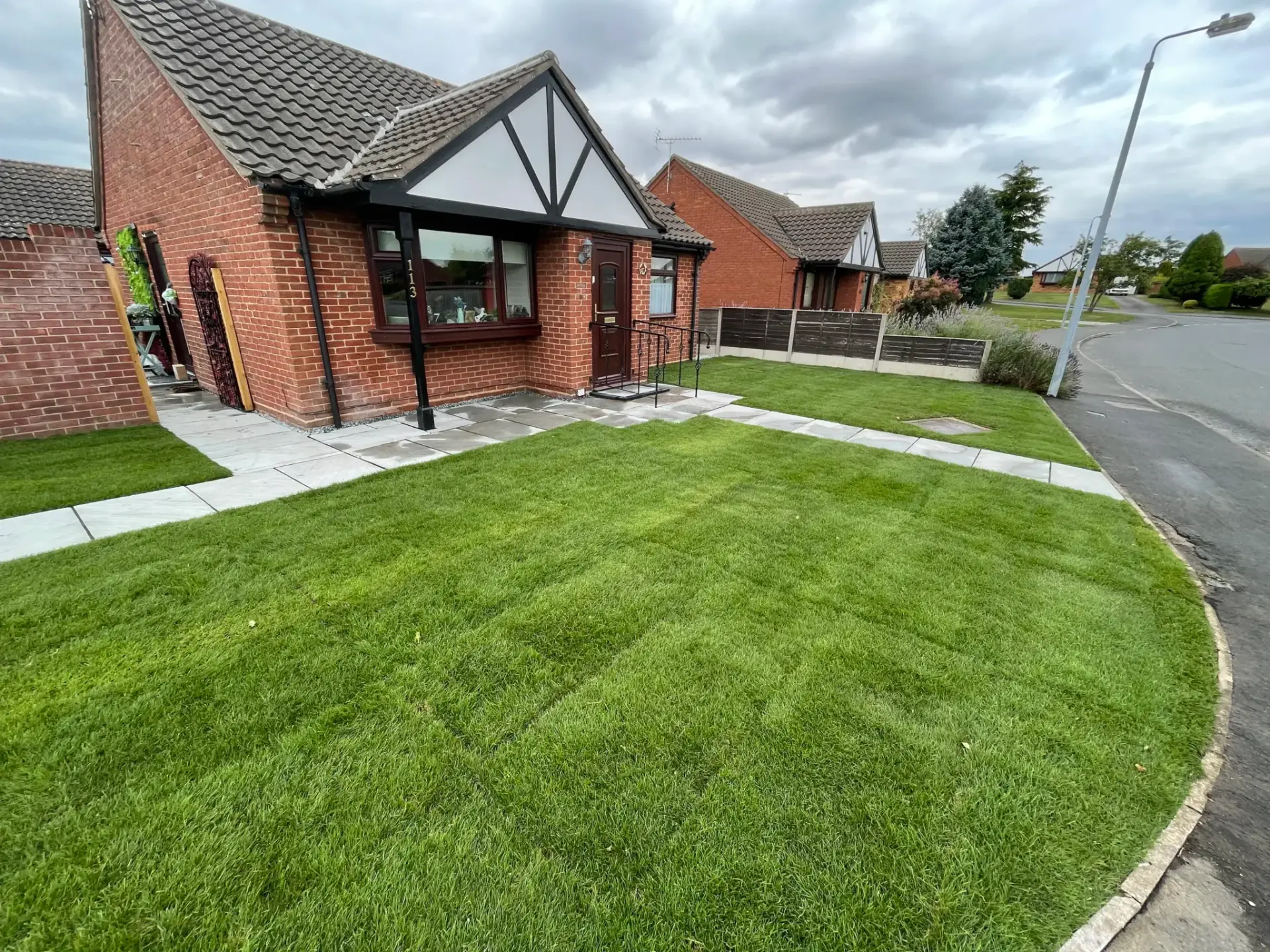 Fresh turf lawn installation in Lincoln by landscapers in Lincoln featuring evenly laid vibrant green grass, clean porcelain paving paths and a red brick bungalow creating a tidy, modern front garden