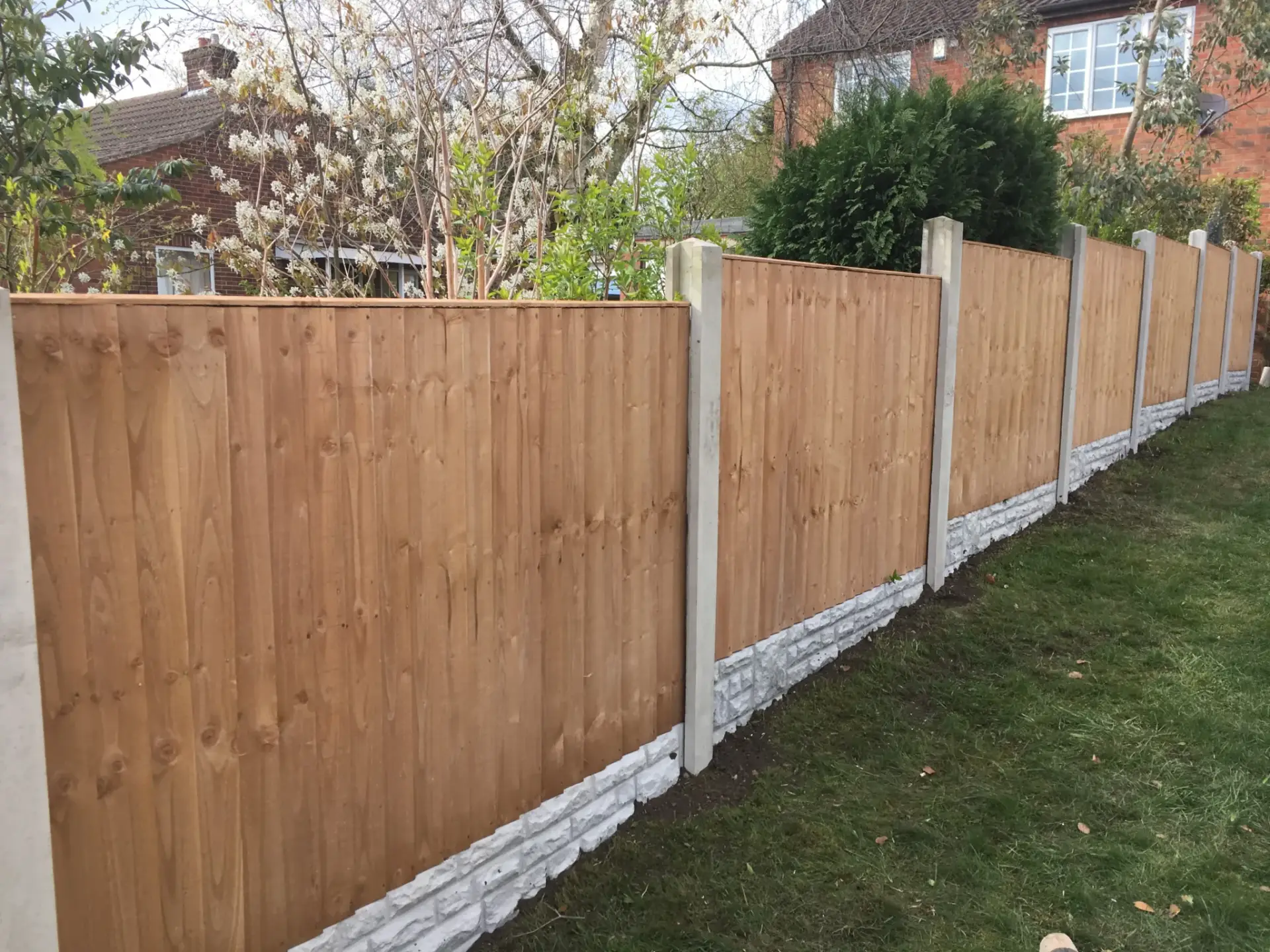 Tan-stained wooden fence panels in Lincoln with concrete posts and decorative white gravel base installed on a raised garden boundary in Lincoln, Lincolnshire — professional garden fencing by garden landscapers in Lincoln.