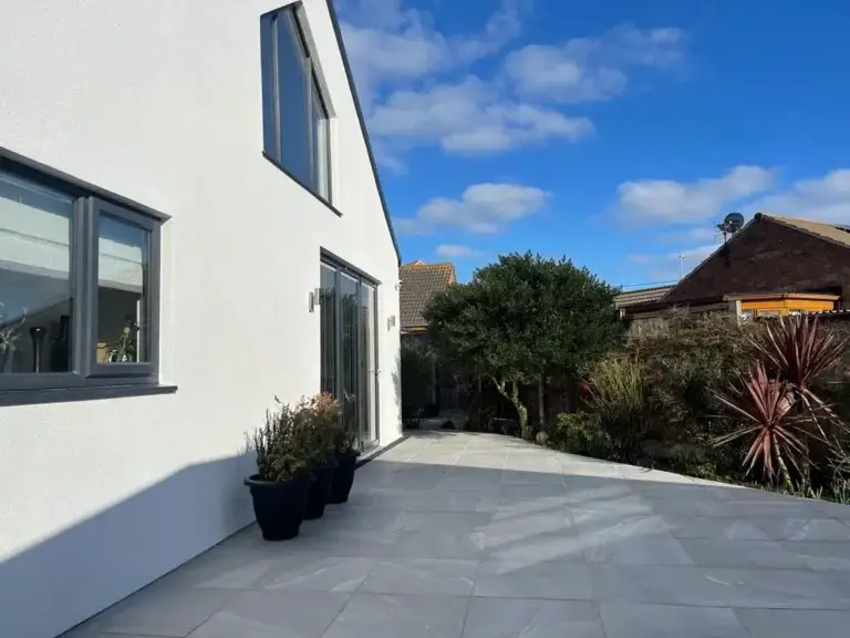 Contemporary light grey porcelain patio beside a white rendered home, framed with potted plants and modern garden borders. Installed by Lincoln based landscape gardeners.