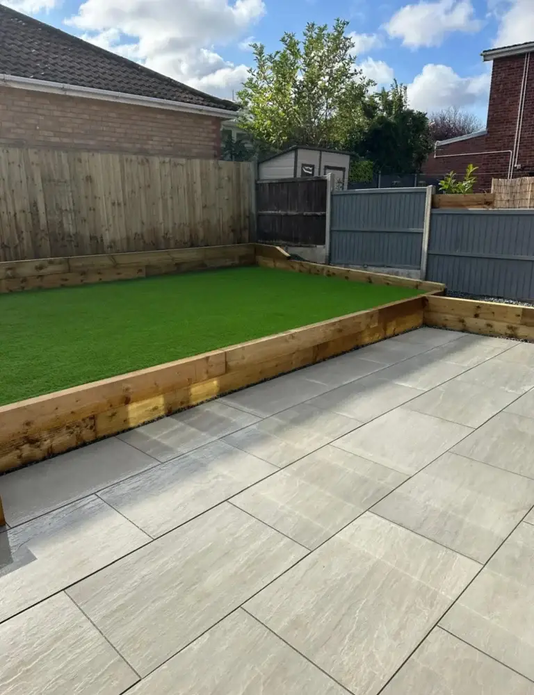 Light beige porcelain patio installation with raised timber sleeper edging and an artificial lawn, creating a clean and low-maintenance garden design. Completed by a Lincoln based landscaper.