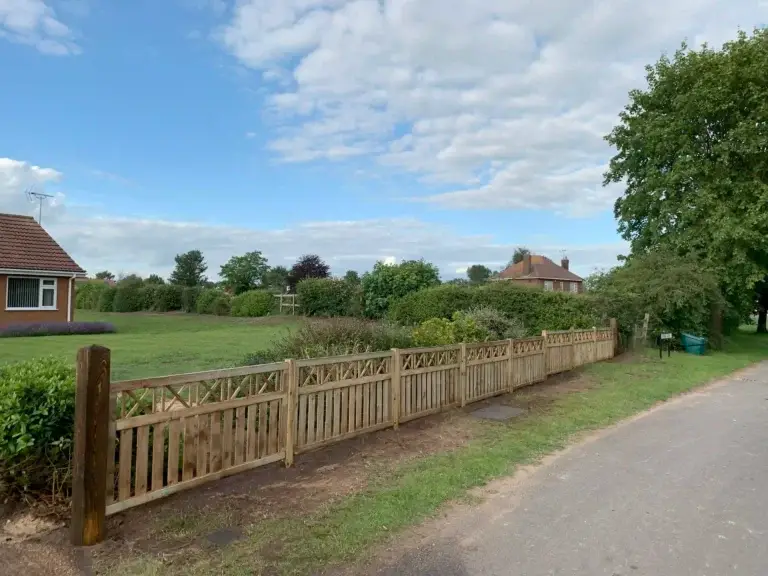 Decorative wooden picket fence installation with lattice top installed along a village roadside garden in Gainsborough, Lincolnshire, bespoke timber fencing by landscapers in Gainborough