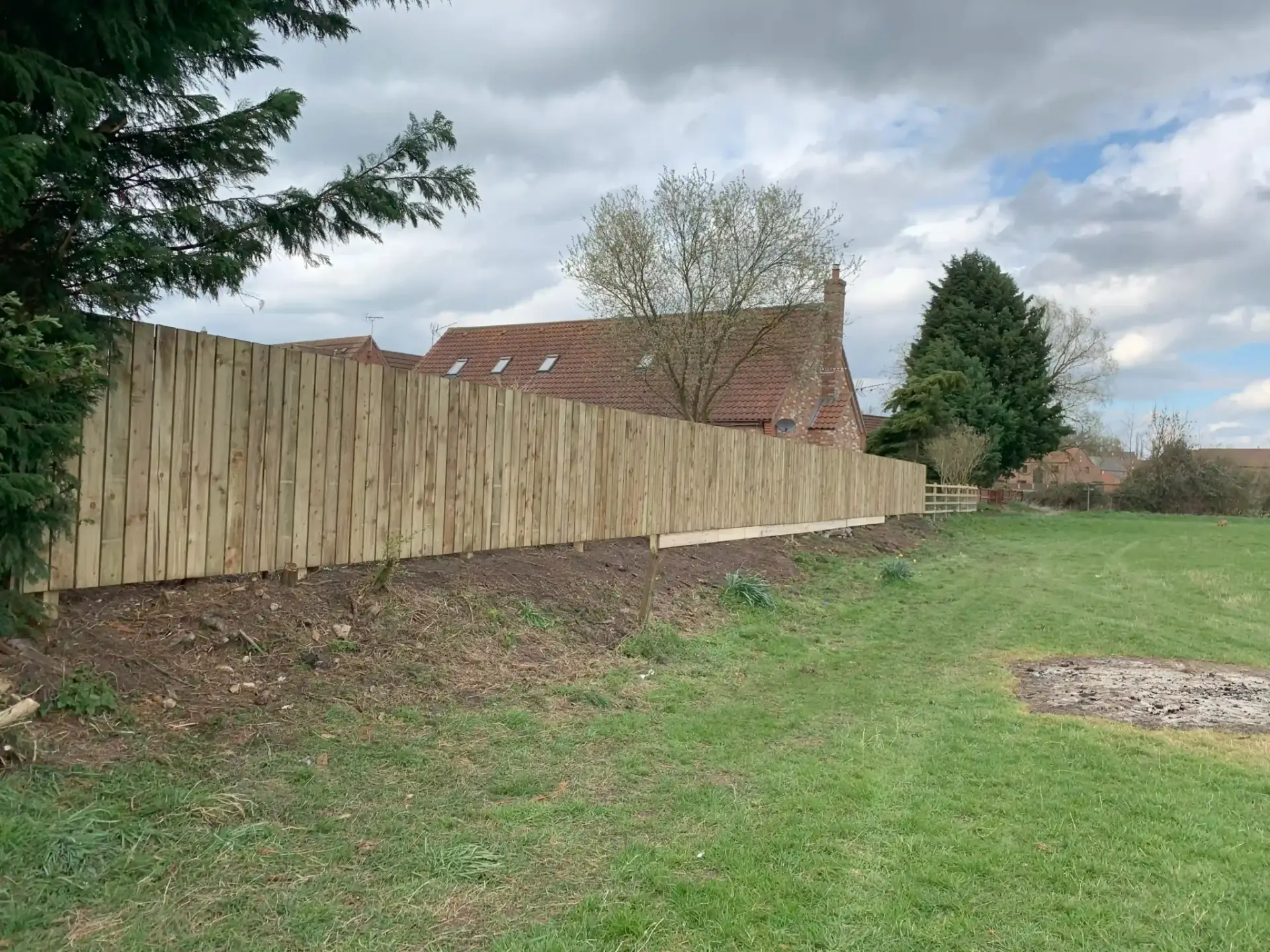 Closeboard timber fencing installation along a raised garden boundary beside a red brick home in The Elms, Torksey, Lincolnshire — professional wooden fence installation by garden landscapers in Lincoln.