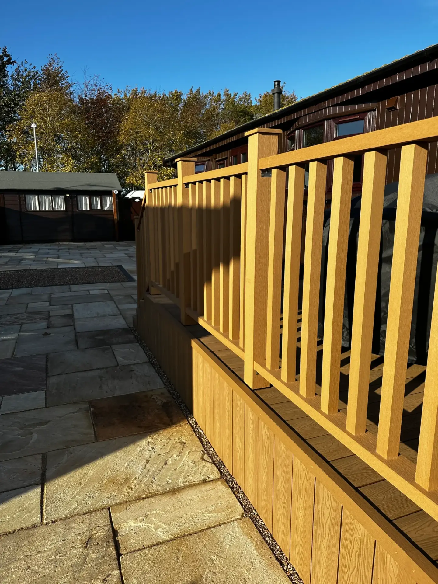 Golden oak composite decking with matching balustrades installed by garden landscapers in Lincoln, adjoining a sandstone patio