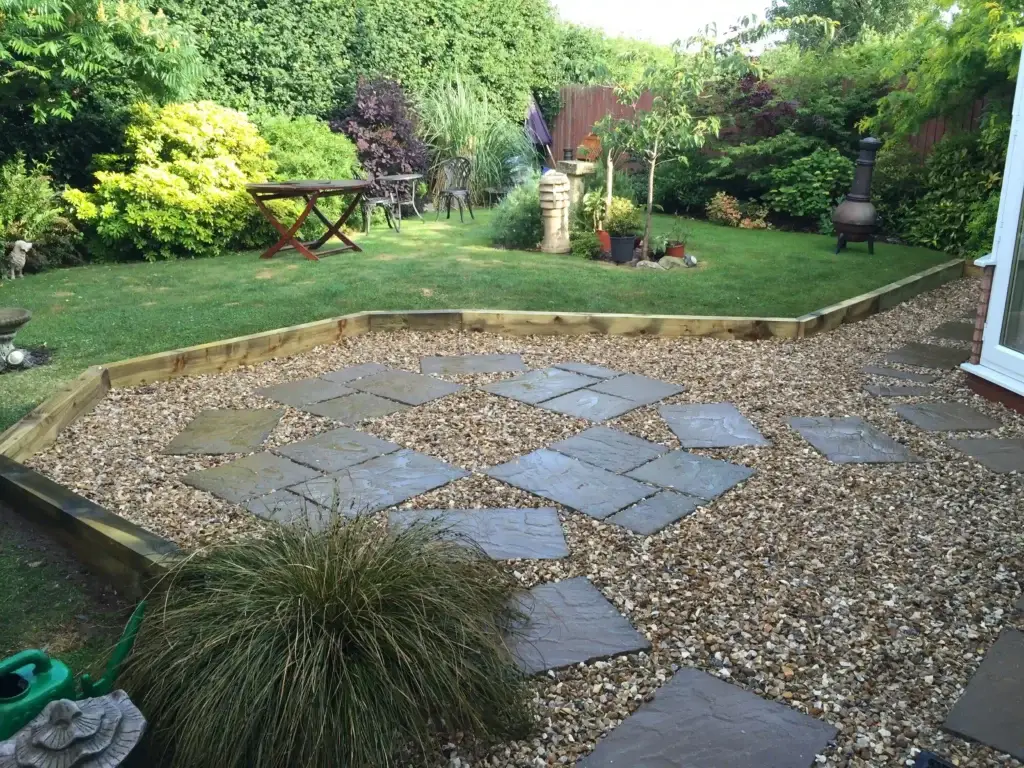 Natural stone and gravel garden design in Lincoln by landscape gardeners featuring rustic paving slabs set within decorative gravel, timber edging and lush planted borders creating a relaxing outdoor seating area