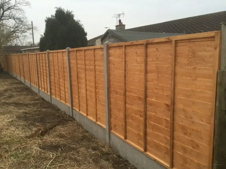 Tan-stained wooden fence panels with concrete posts and gravel boards installed in a large residential garden in Lincolnshire, professional fencing installation by landscapers in Lincoln