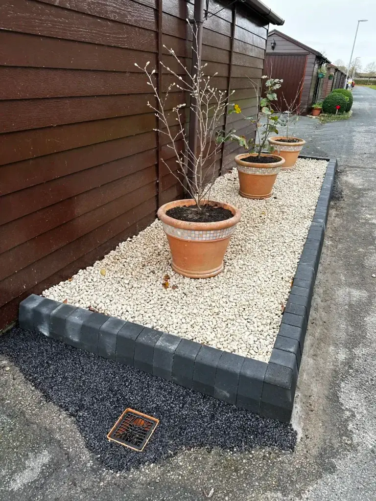 Decorative gravel border installation by landscapers in Lincoln featuring light golden gravel, charcoal block edging and terracotta plant pots creating a neat and low maintenance planting area beside wooden lodges