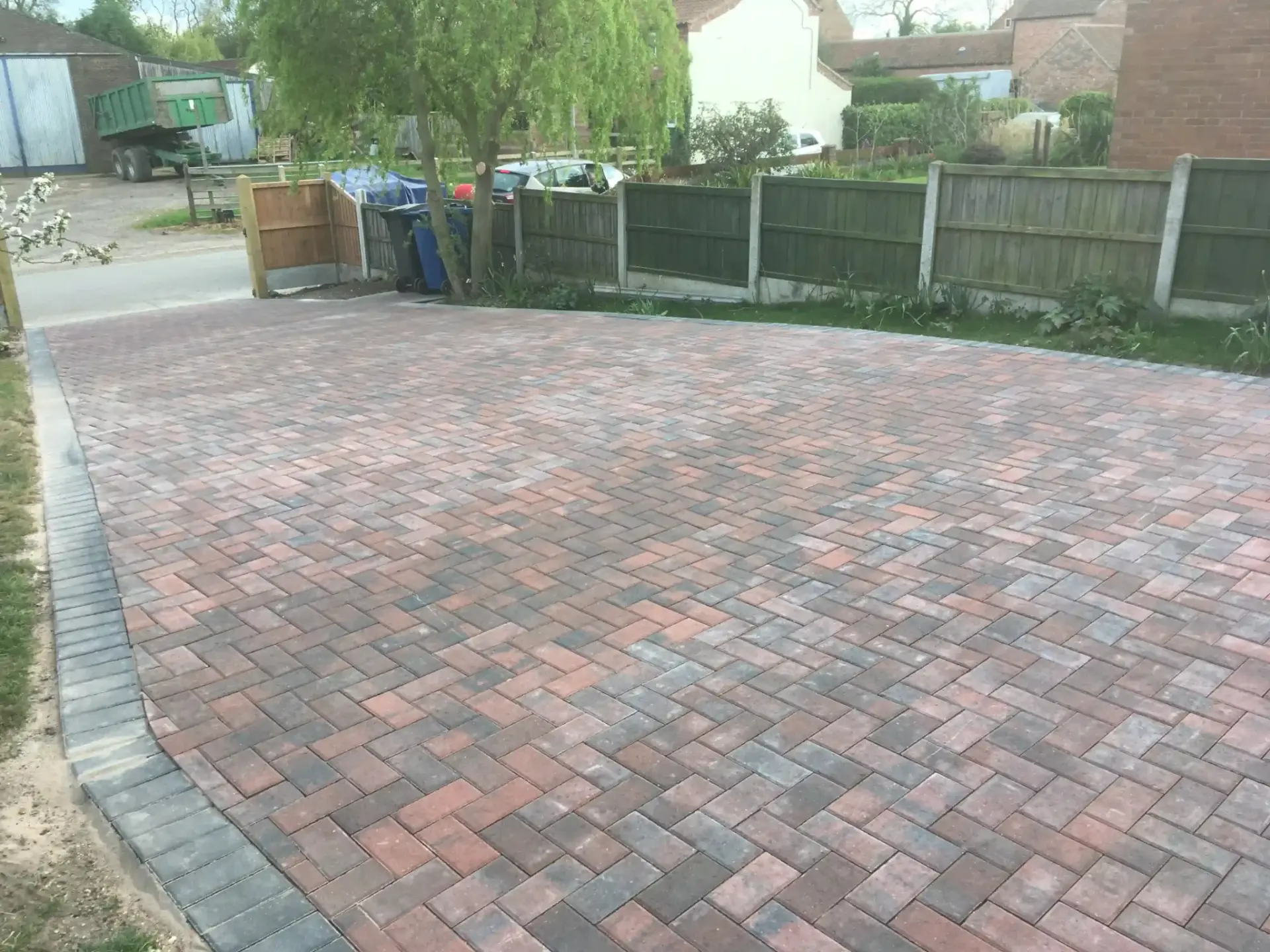 Block paving driveway installation by landscapers in Lincoln featuring red and charcoal pavers in a herringbone pattern with clean grey edging stones creating a durable and modern entrance finish