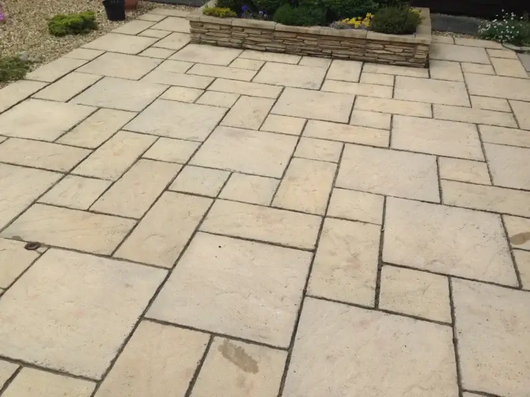 Cream sandstone patio installation with a traditional block pattern and raised stone planter, creating a timeless and durable outdoor surface. Completed by landscape gardeners in Saxilby, Lincolnshire.