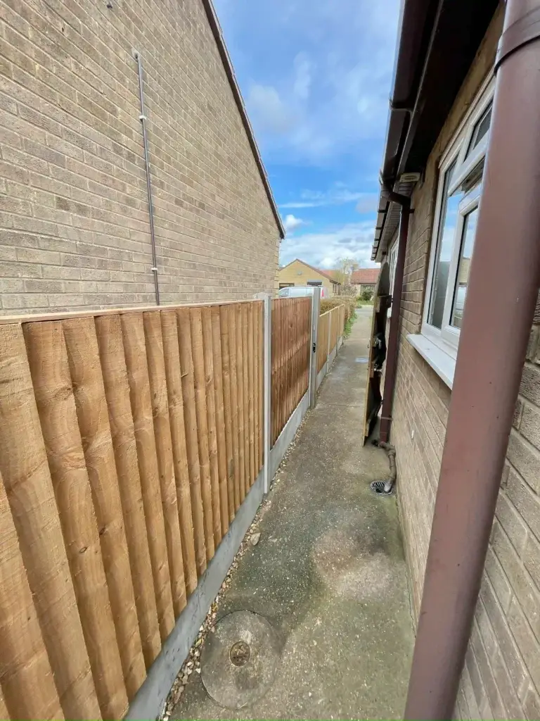 Round-top timber fence panels with concrete posts installed along a narrow side path between two brick houses in Lincolnshire, garden fencing by landscapers in Lincoln
