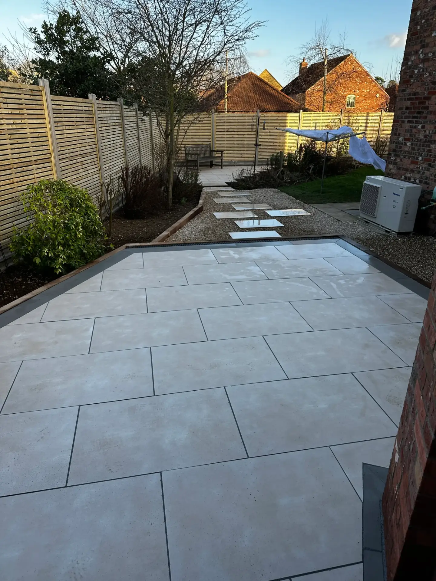 Porcelain patio and stepping stone path installation in Lincoln by landscape gardeners featuring light cream paving with charcoal edging, gravel borders, and a modern walkway leading through landscaped garden areas