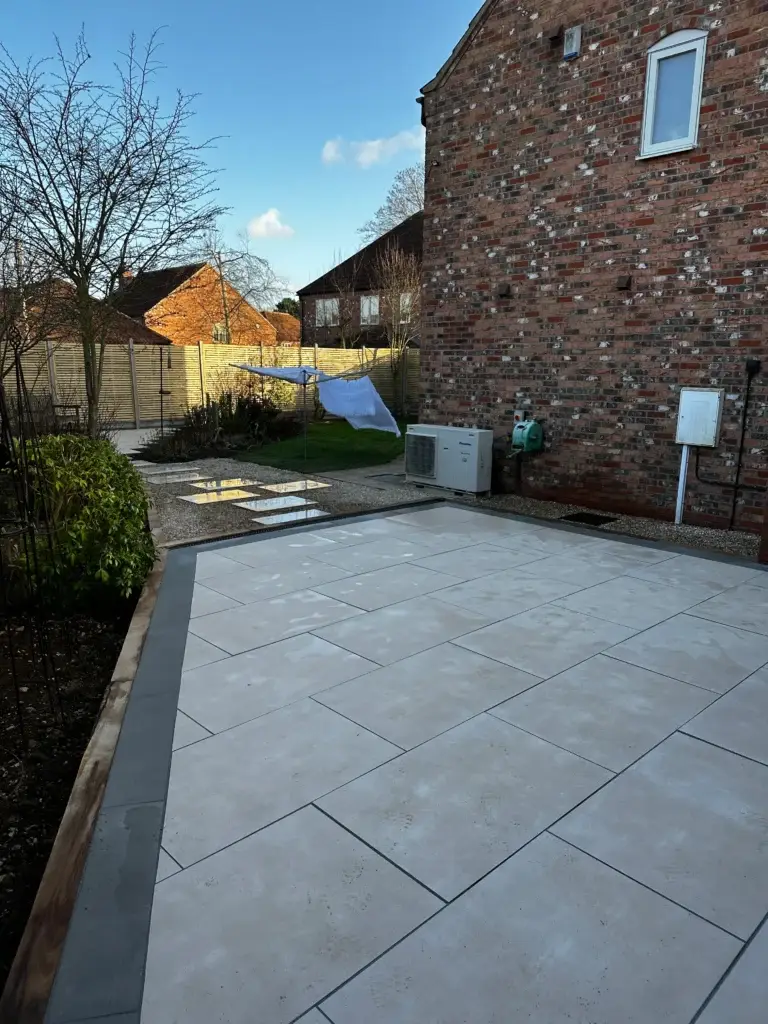 Porcelain patio installation in Lincoln by landscapers in Lincoln featuring smooth light beige paving slabs with precise dark edging, modern brick property backdrop and landscaped garden borders for a clean outdoor living space