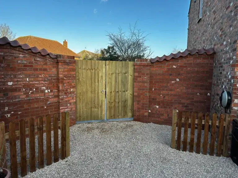 Timber double gate with natural wooden finish set between two red brick walls and gravel driveway installation by landscapers in Lincoln.