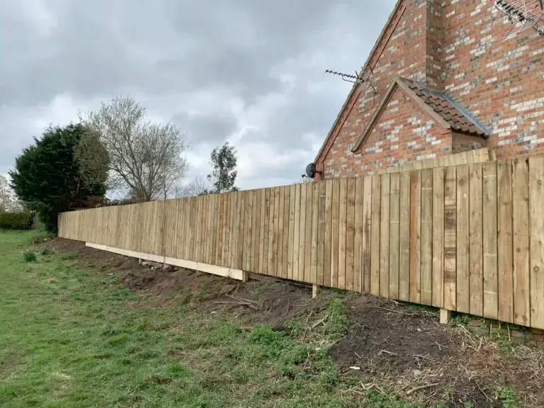 Long stretch of closeboard wooden fencing installation along a sloped garden boundary beside a red brick property in Lincolnshire, timber fence installation by landscapers in Lincoln