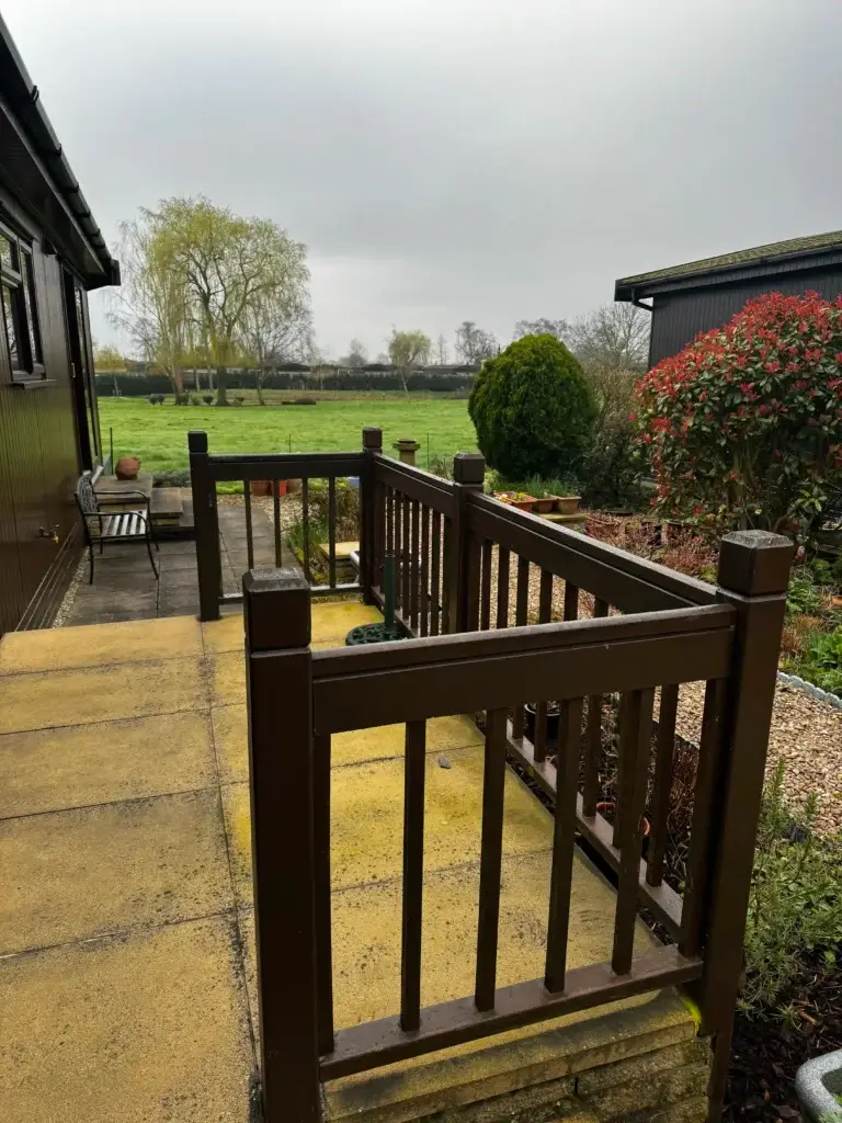 Dark brown wooden handrail and balustrade installation on a raised beige sandstone patio overlooking landscaped gardens at The Elms, Torksey, Lincolnshire, outdoor decking feature by landscapers in Lincoln