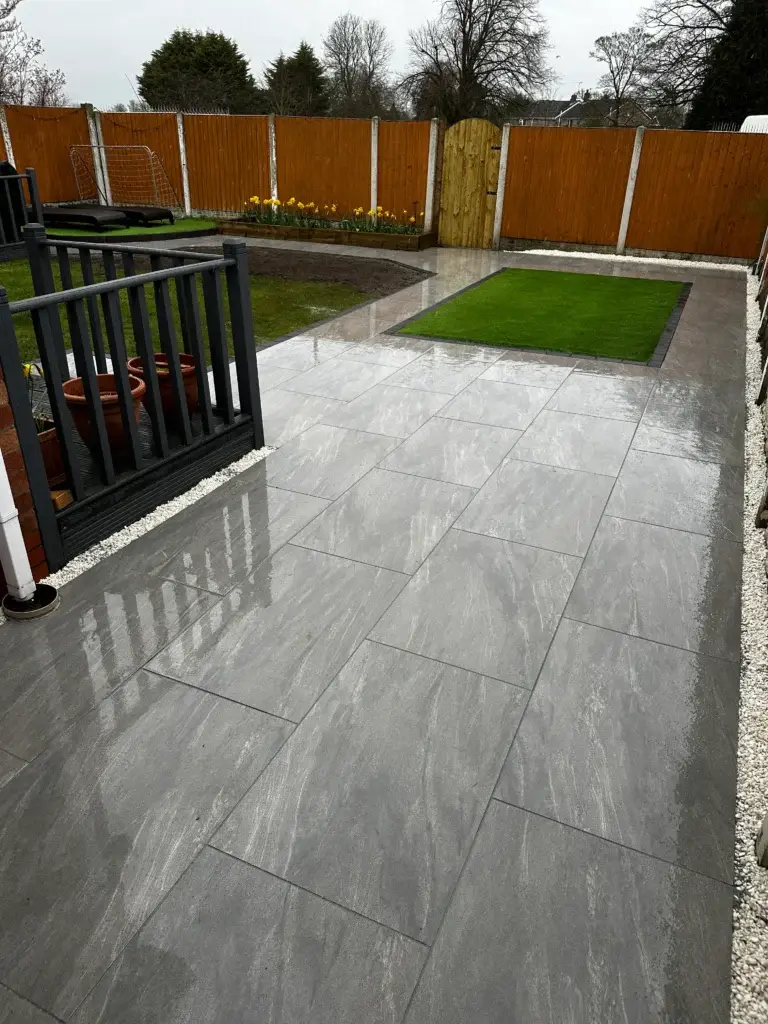 Modern grey porcelain patio installation with high-gloss tiles and precise jointing, contrasting against rich green turf and timber fencing. Completed by landscape gardeners in Gainsborough, Lincolnshire.