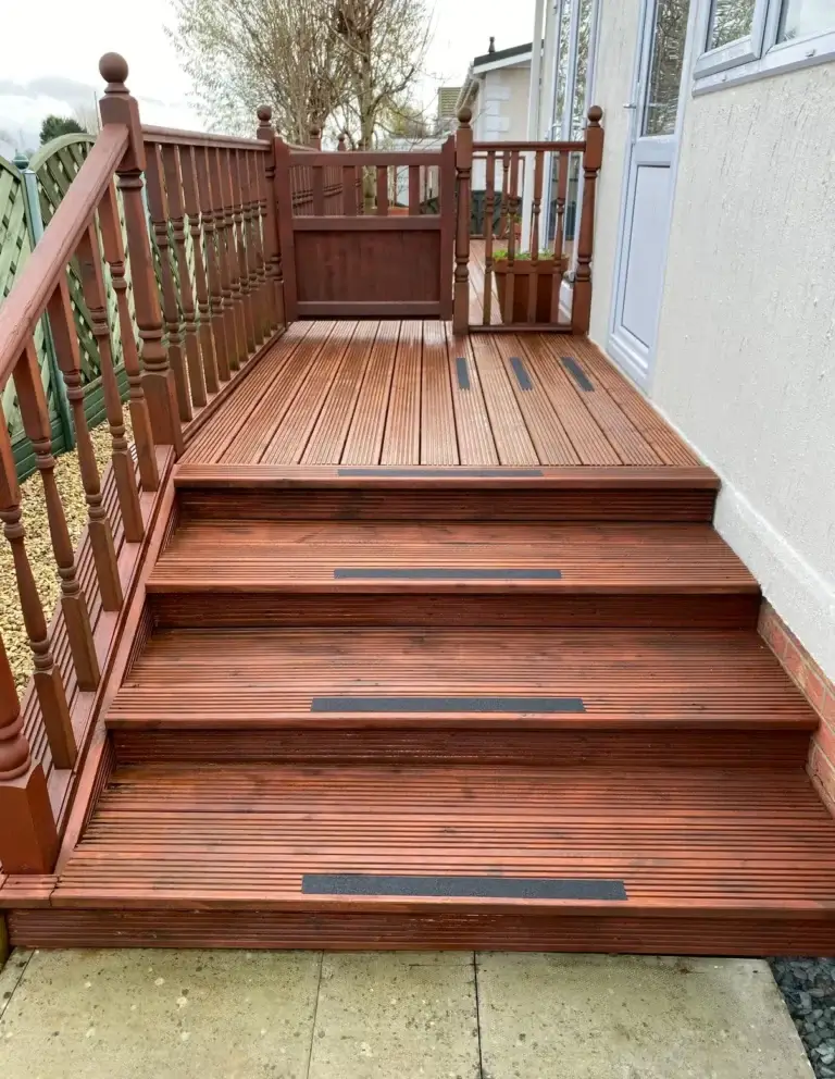 Wooden decking with steps and handrails installed by landscapers in Lincoln, featuring anti-slip inserts and a rich stained finish