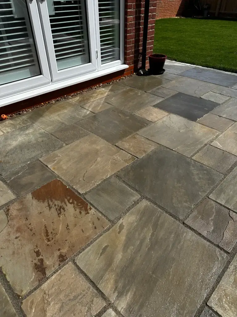 Natural Indian sandstone patio in mixed brown and grey tones with a hand-cut surface, laid beside French doors leading onto a fresh green lawn. Completed by Lincoln based garden landscapers.