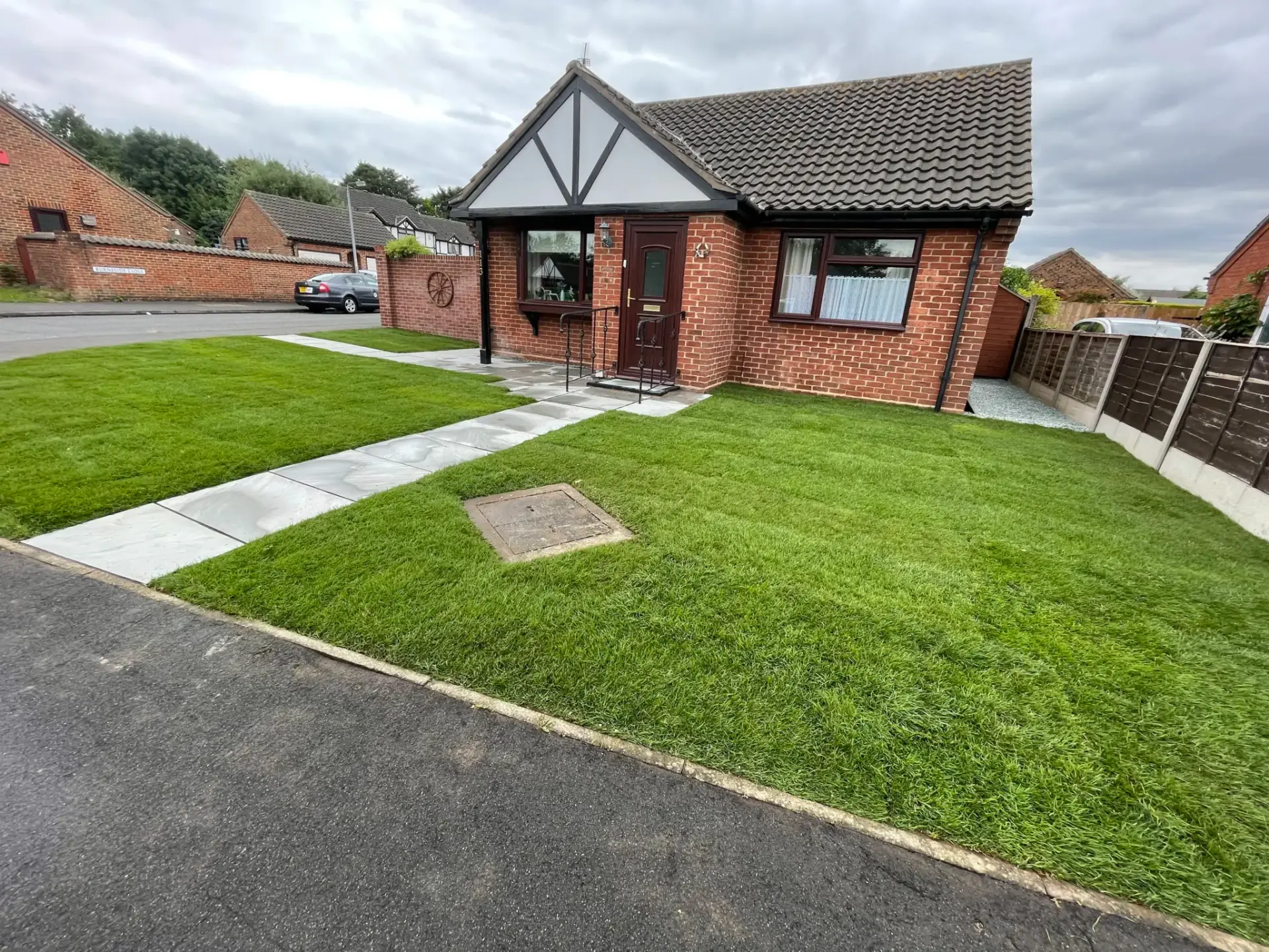Turf lawn installation in Lincoln by landscape gardeners featuring freshly laid green grass with clean straight edges, grey porcelain paving paths and a red brick bungalow for a neat and modern finish