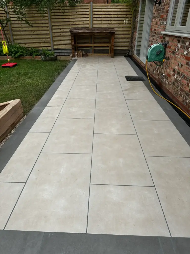 Porcelain patio installation in a modern garden in Lincoln by landscape gardeners featuring pale grey large-format paving slabs and a sleek low-maintenance layout under a blue sky