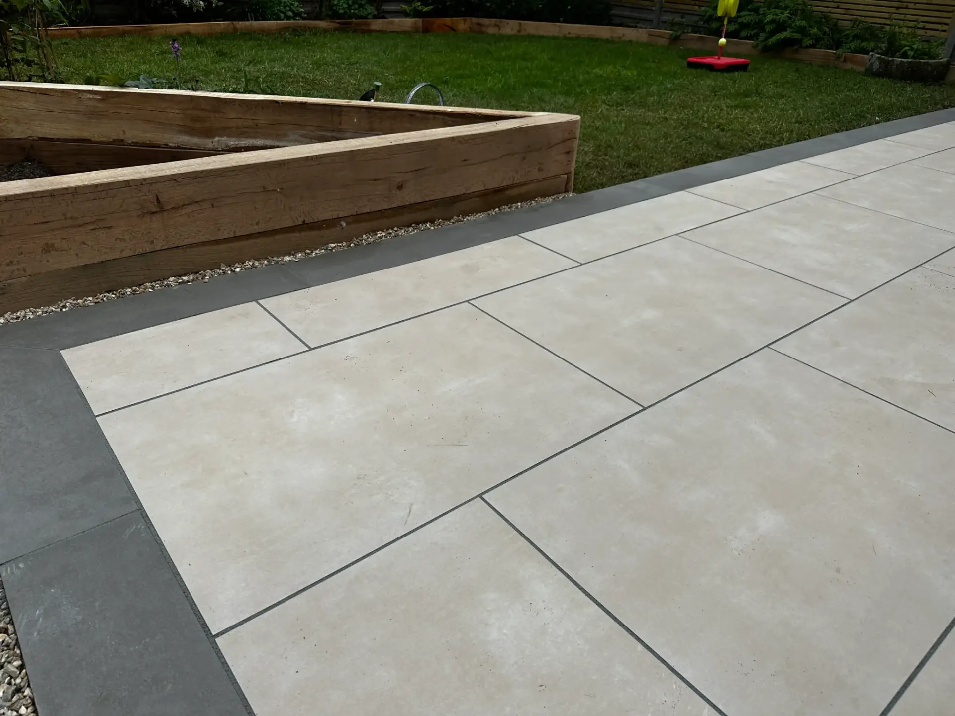 Porcelain patio installation in Saxilby by Reshape Landscaping featuring light cream paving slabs with charcoal grey edging and raised timber sleeper beds for a clean, modern garden design