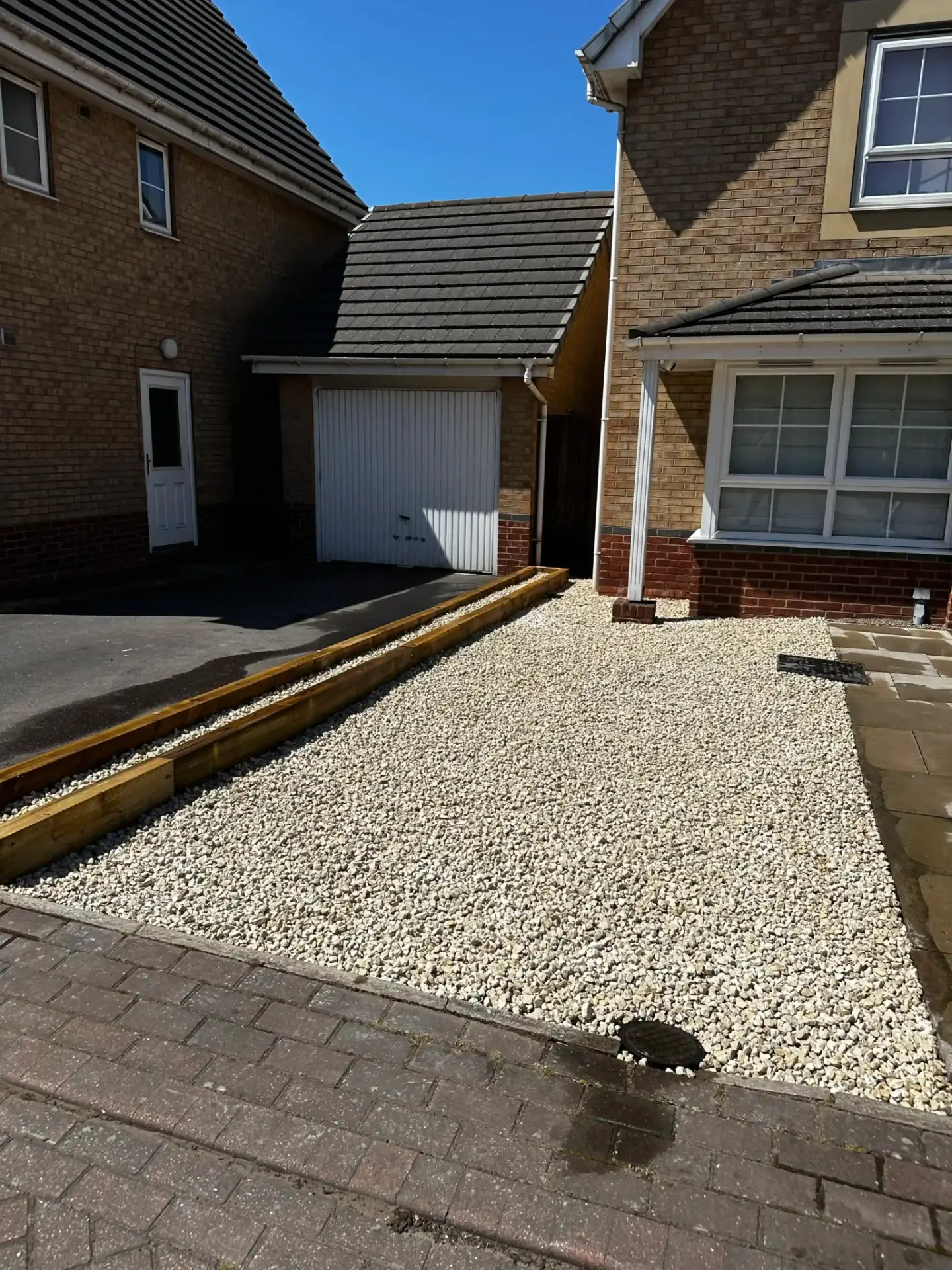Gravel driveway installation by landscapers in Lincoln featuring light cream decorative gravel bordered with timber sleepers and block paving, creating a clean and modern low maintenance front garden