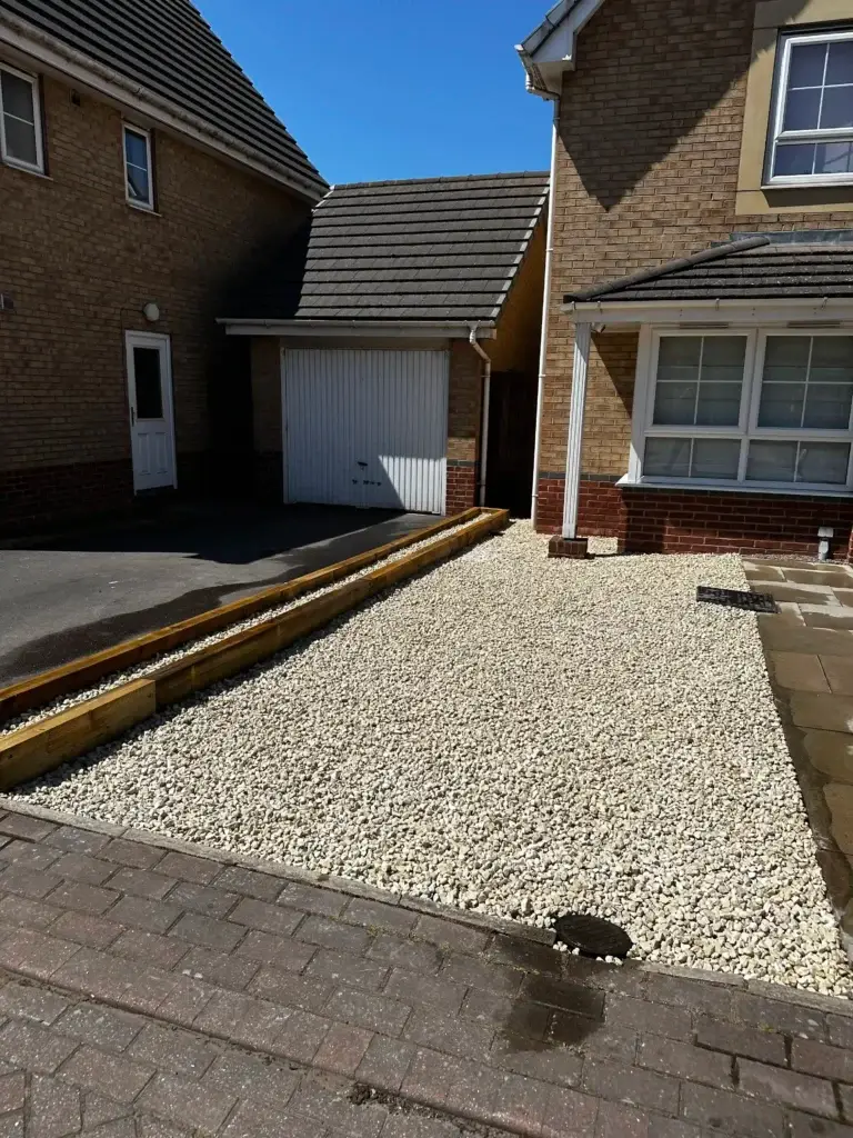 Gravel driveway installation by landscapers in Lincoln featuring light cream decorative gravel bordered with timber sleepers and block paving, creating a clean and modern low maintenance front garden