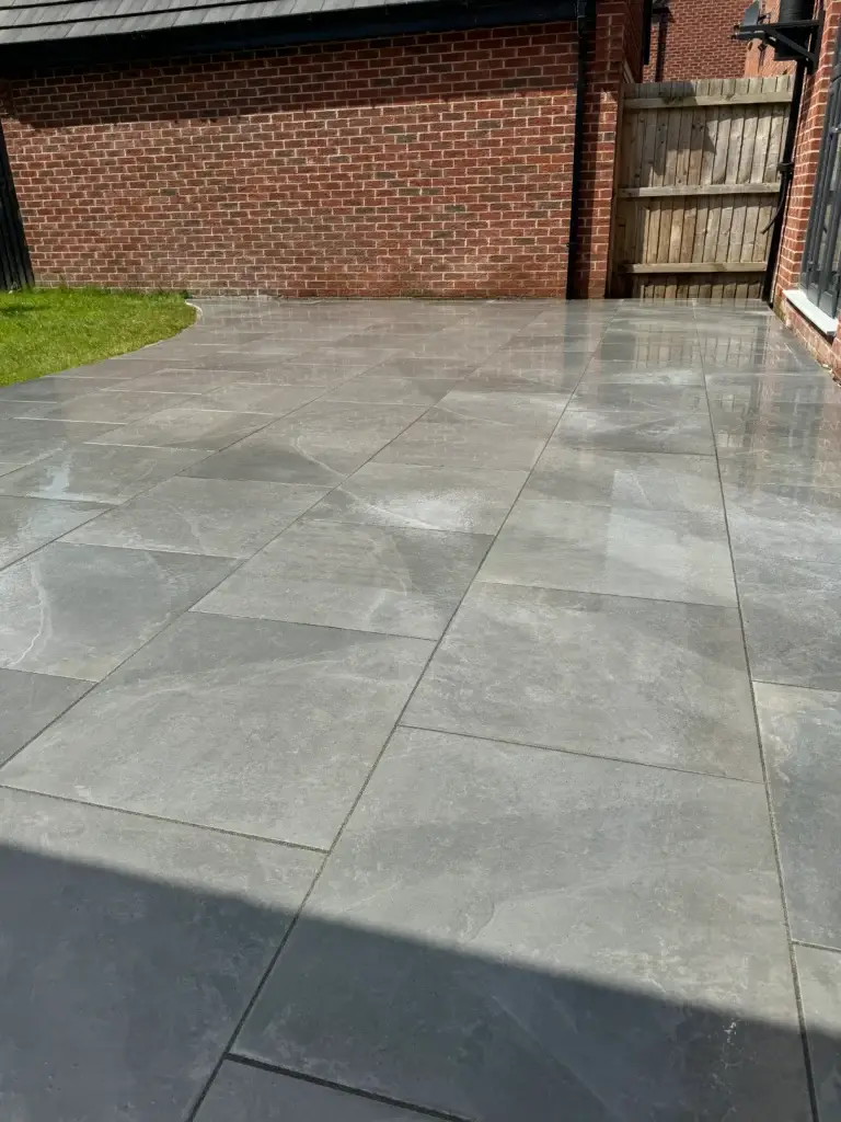 Sleek grey porcelain patio installation beside a red brick house, finished with smooth joint lines and a reflective modern surface. Completed by landscapers in Gainsborough, Lincolnshire.