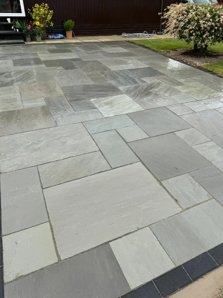 Contemporary grey sandstone patio installation with dark border detailing and mixed stone tones, providing a sleek modern finish to a landscaped garden. Completed by garden landscapers in Saxilby, Lincolnshire.