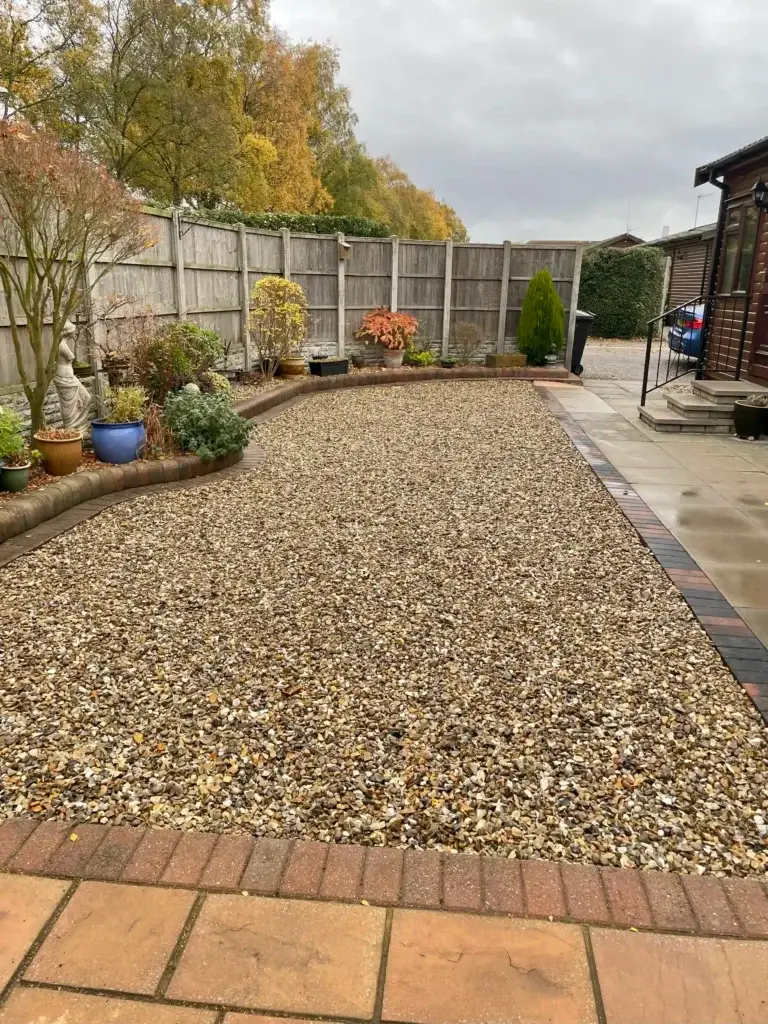Decorative gravel garden design by landscapers in Lincoln featuring golden pea gravel, brick edging borders, porcelain paving paths and colourful potted plants for a low maintenance modern outdoor space