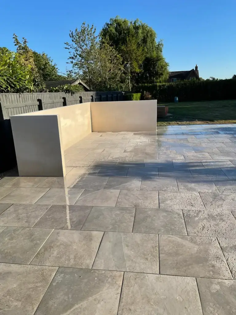 Porcelain patio installation in Lincoln by garden landscapers featuring light beige paving slabs with subtle texture, integrated rendered seating walls and a smooth reflective finish for a premium modern garden