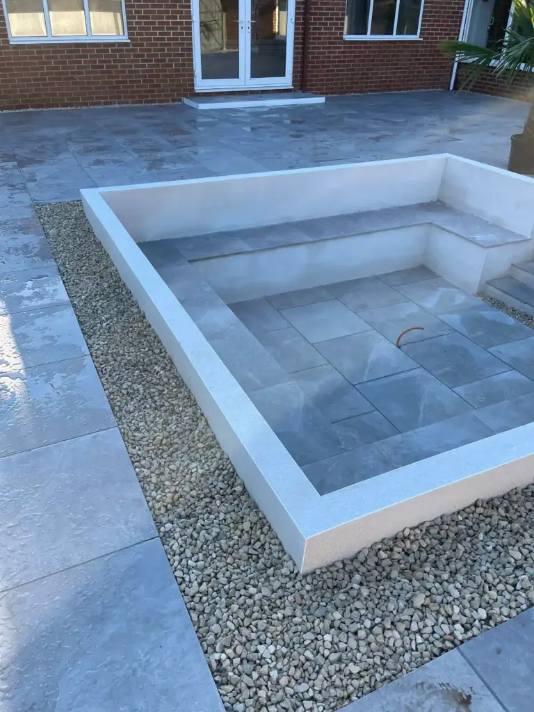Modern porcelain firepit installation in Lincoln Landscape gardeners featuring a sunken seating area with smooth grey tiles, white rendered walls, and decorative gravel edging for a contemporary outdoor design