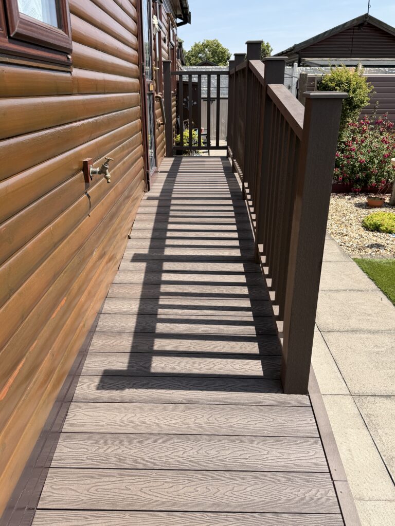 Composite decking walkway with matching balustrade alongside a log-clad park home – park home decking Lincolnshire