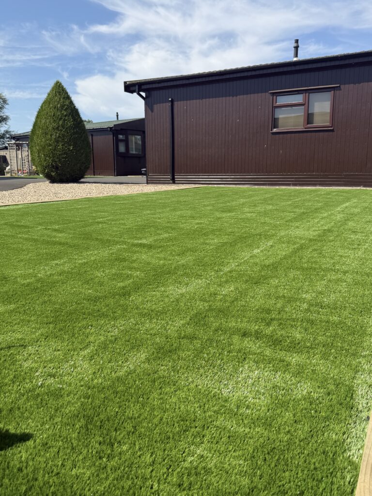 Artificial grass lawn with gravel border beside a timber lodge, laid by landscape gardeners in Lincoln