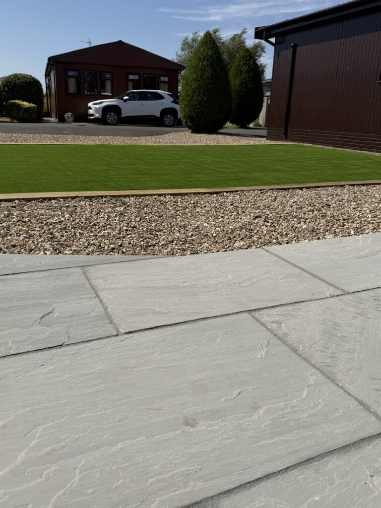 Grey riven paving laid beside gravel and a new artificial lawn, patio installation by landscapers covering Lincolnshire