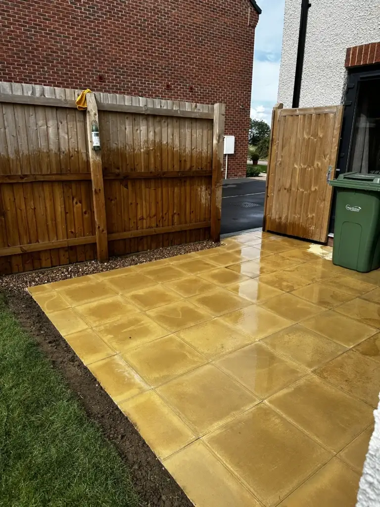 Buff sandstone patio installation beside a red brick home and wooden fencing, laid with clean straight joints and smooth edges for a modern finish. Completed by Lincoln based landscape gardeners.