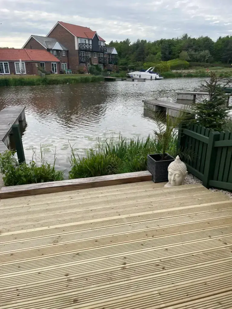 Wooden decking installation in Lincoln by landscapers in Lincoln overlooking a lakeside garden, featuring grooved anti-slip boards and green fencing