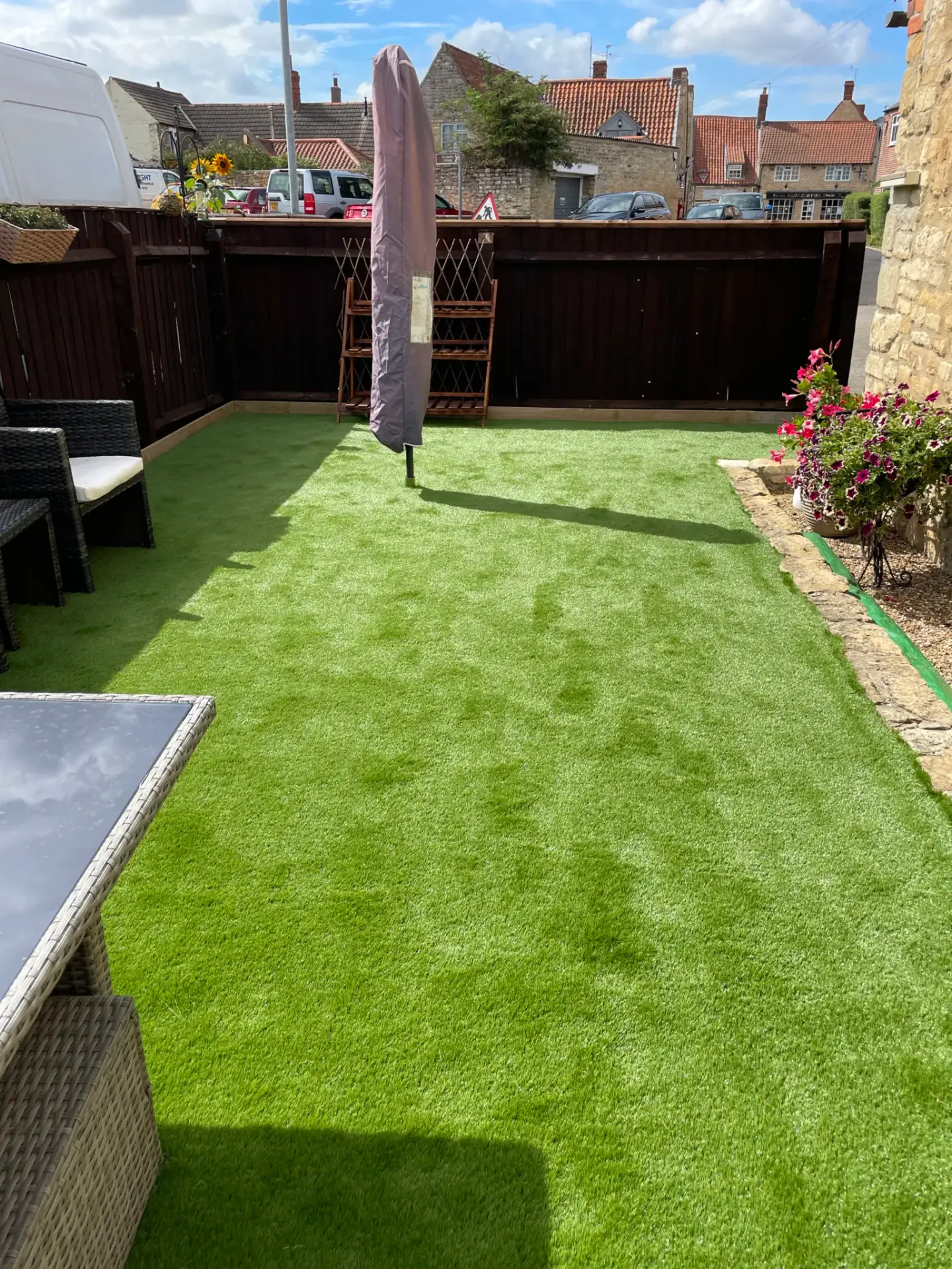 Artificial grass installation in Lincoln by landscape gardeners featuring bright green low maintenance turf, dark wooden fencing, rattan garden furniture and a paved seating area under a parasol