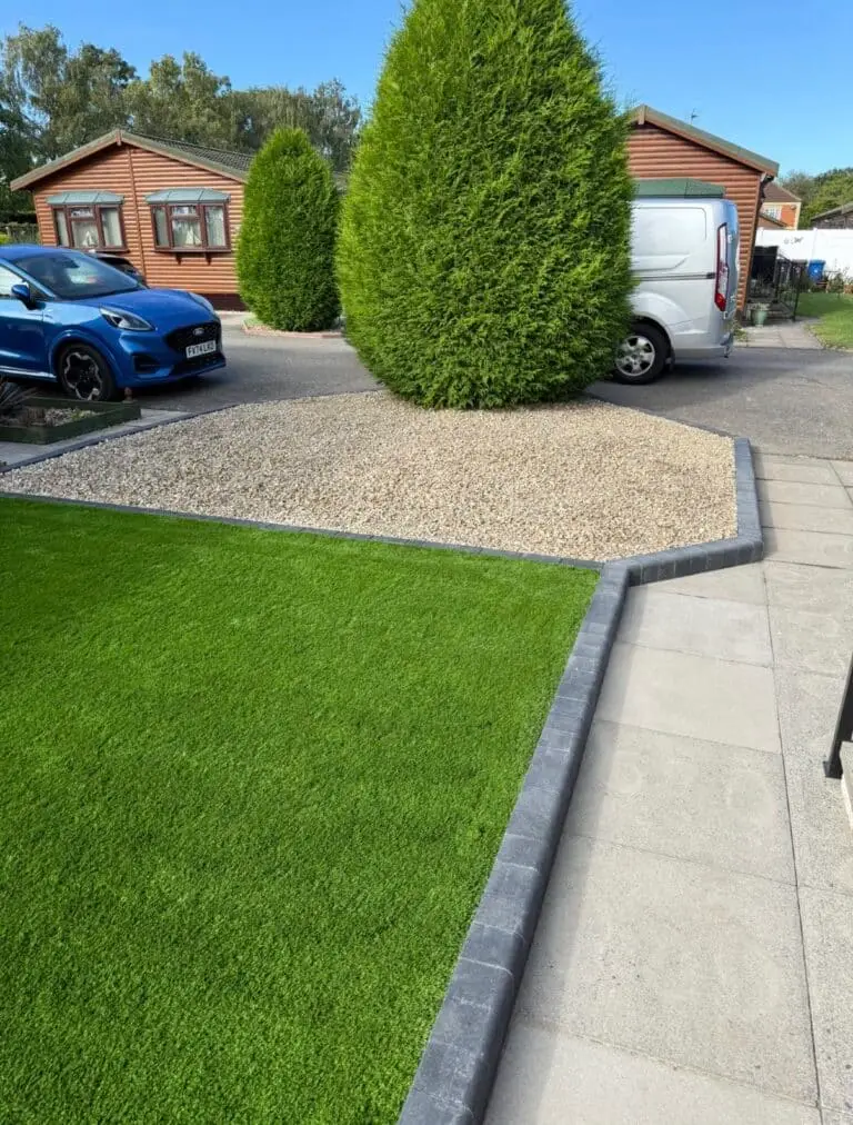 Artificial grass installation in Lincoln by landscape gardeners, featuring lush artificial grass edged with dark grey kerb blocks, decorative gravel drive, and neat porcelain paving beside wooden lodge units.