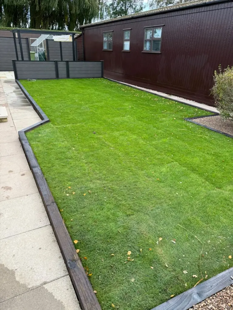 New turf lawn installation at The Elms Torksey by landscapers in Lincoln featuring fresh green grass, dark timber edging and smooth paving alongside modern lodge-style homes with grey fencing