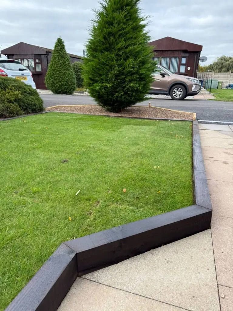 Fresh lawn installation at The Elms Torksey by landscapers in Lincoln, featuring neatly laid natural turf with dark grey kerb edging, light paving and modern timber lodges in the background