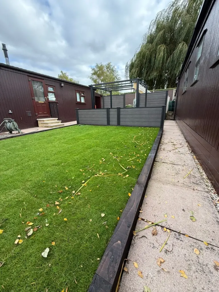 Real lawn installation and raised sleeper garden at The Elms Torksey by landscape gardeners in lincoln featuring lush green synthetic turf, dark timber edging, and modern grey fencing with a stylish pergola seating area