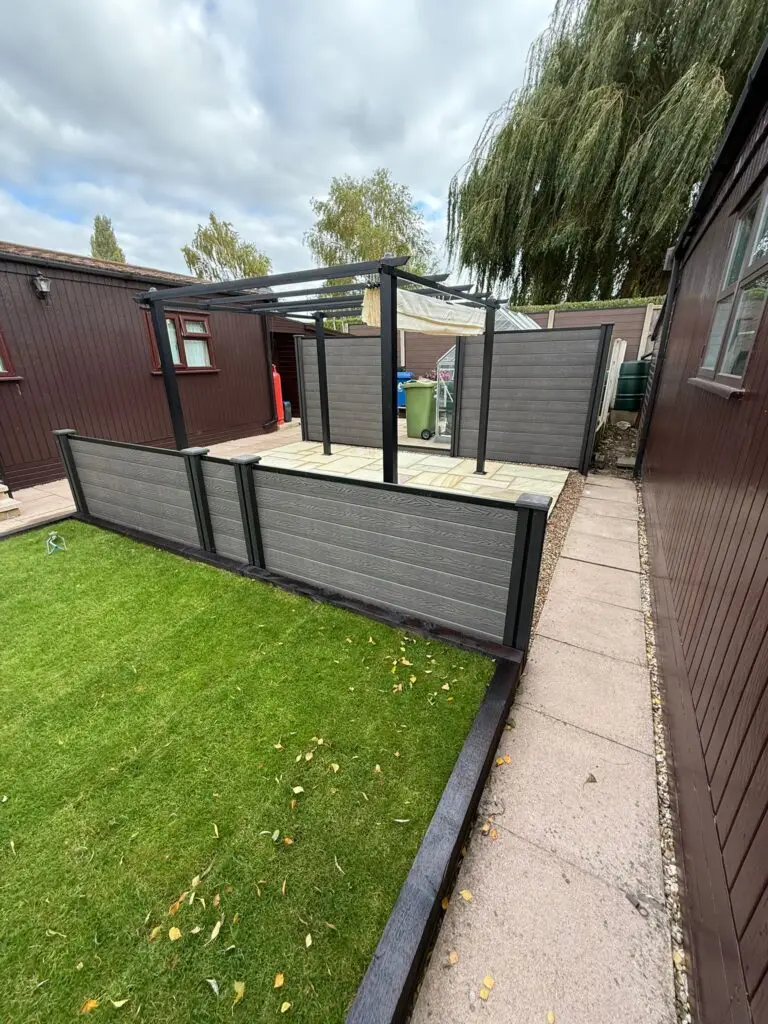 Composite grey raised patio with dark aluminium framing and modern pergola structure installed by landscapers in Lincoln. Contemporary garden renovation with paved seating area and neat lawn edging