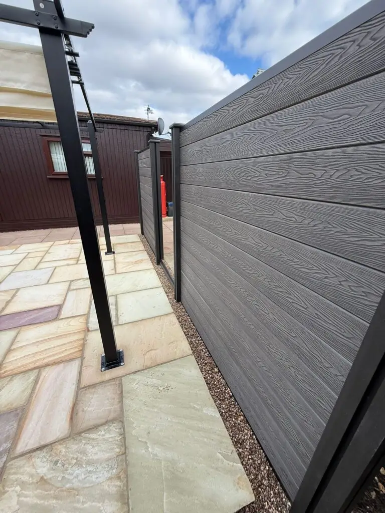 Close-up of grey composite privacy fencing with black aluminium posts and sandstone patio paving, installed by landscapers in Lincoln. Modern low-maintenance garden design.