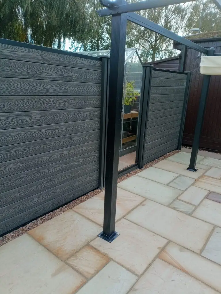 Modern composite grey fence panels with black steel pergola posts and light sandstone patio installation landscapers in Lincoln. Contemporary low-maintenance garden design.