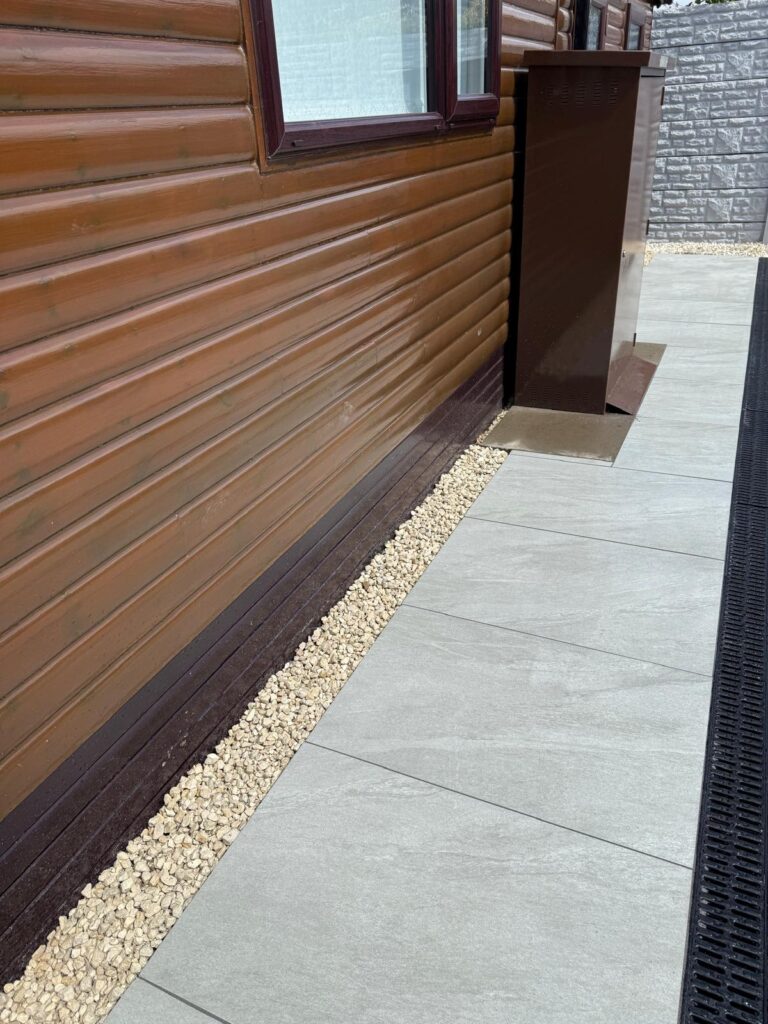 Grey porcelain pathway in Lincoln beside timber-effect cladding, with cream gravel edging and black linear drainage.