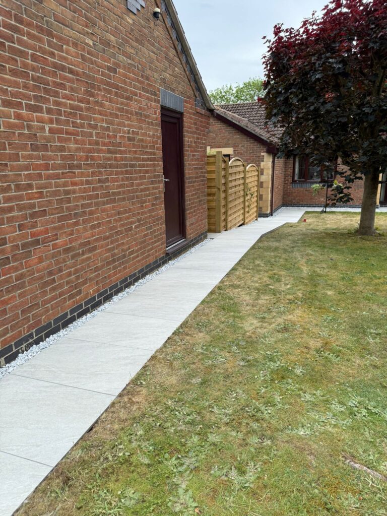 Grey porcelain paving path with light gravel mowing strip running alongside a brick bungalow in Lincolnshire, installed by Reshape Landscaping