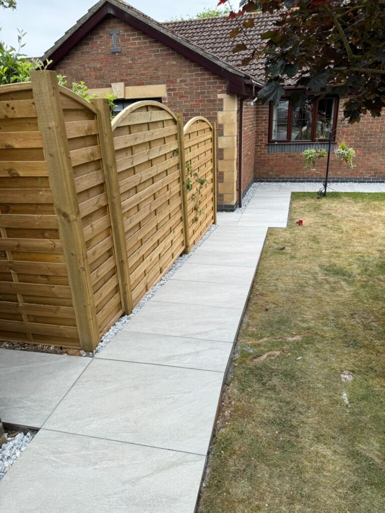Light grey porcelain garden path beside curved-top timber fence panels and gravel border, professional landscaping in Lincolnshire