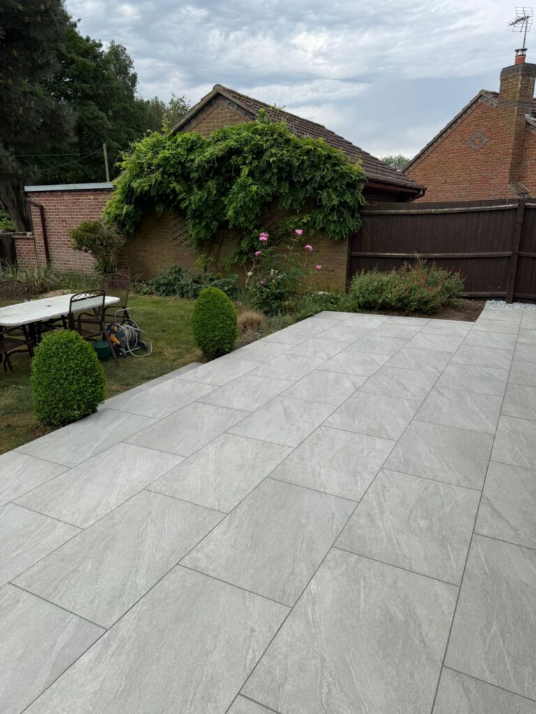 Narrow grey porcelain side-return path with gravel edging viewed through a timber gate, garden landscaping in Lincolnshire