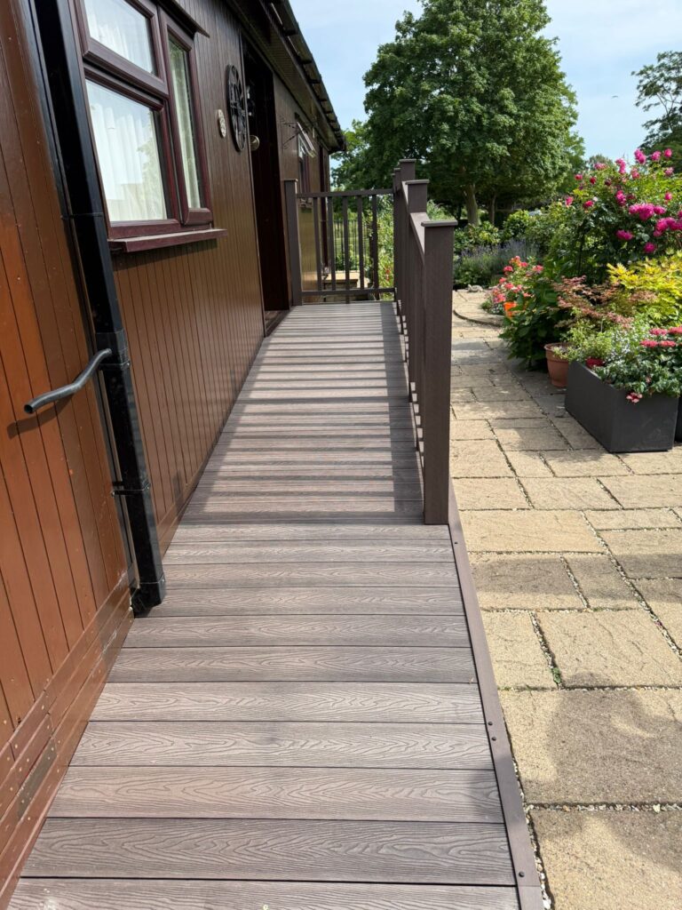 Grey composite decking walkway with safety balustrade installed beside a holiday lodge and landscaped garden