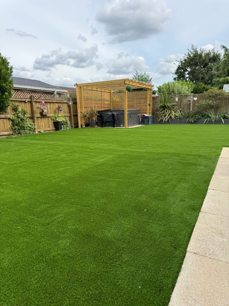 Artificial lawn surrounding a timber pergola and hot tub in a landscaped Lincoln garden